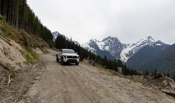 Toyota Tacoma Driving on Mountain Road with Snow-Capped Peaks in Background
