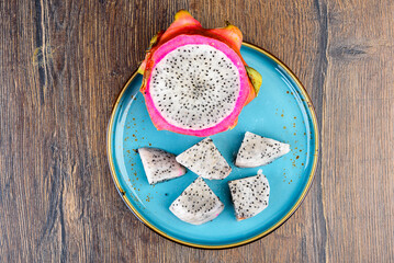 Half of Dragon Fruit and pieces of pulp on a blue plate.