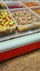 Colorful display of fresh vegetables and mushrooms in clear containers at a market. Various ingredients are arranged neatly for sale.