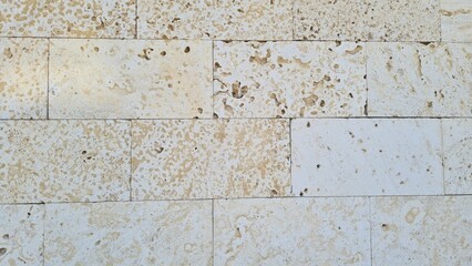 Textured stone wall with light beige and cream colors. The surface shows natural patterns and variations, suitable for backgrounds or architectural concepts.