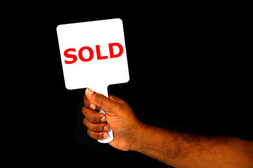 Hand holding SOLD sign board with black background close-up view 