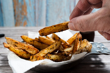 Hand selecting crispy seasoned potato wedges from a rustic serving platter.