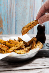 Person grabbing freshly-baked seasoned potato wedges from a ceramic dish