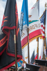 Multiple flags are displayed, including the California state flag and an American flag, held by individuals in uniform.
