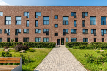 A modern brick apartment building with a landscaped garden and a path on a sunny day.