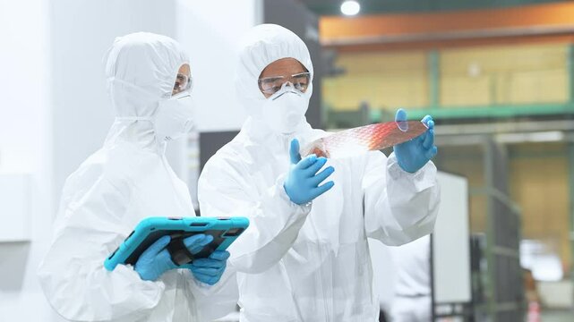 半導体工場でタブレットを持ってシリコンウエハーを検査する防護服を着た男女作業員