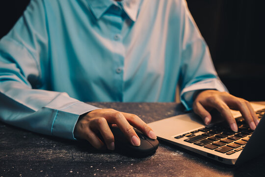 businessman working. Professional person in blue shirt using laptop with computer mouse on wooden table in low light setting - Powered by Adobe