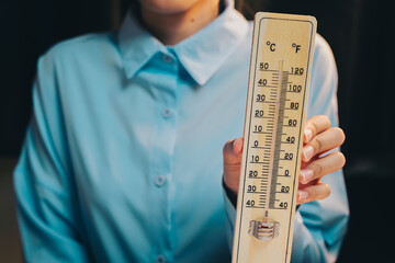 Thermometer concept. Woman in Blue Shirt Holding Wooden Thermometer with Temperature Scale in Studio Environment