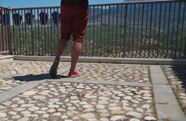 Man Walking Near Fenced Balcony Overlooking Panoramic Mountain Landscape