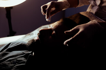 Relaxed young man having various beauty treatments at a beautician; Portrait of a man with a beard having beauty injections and face masks