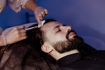 Relaxed young man having various beauty treatments at a beautician; Portrait of a man with a beard having beauty injections and face masks