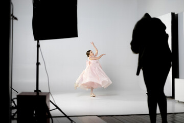 A young girl in a pink dress poses gracefully in a photography studio.