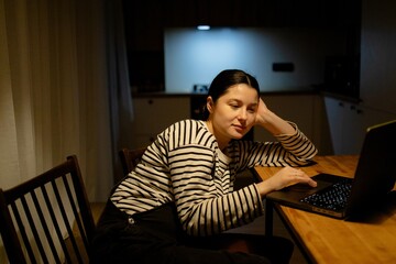 A woman sitting at a table with a laptop. She is wearing a striped shirt and has her hair tied...