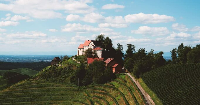 Schloss Staufenberg sits atop a lush hillside vineyard near Durbach, with terraced grapevines and red-roofed buildings beneath a dramatic sky in this scenic cinematic aerial view of German countryside