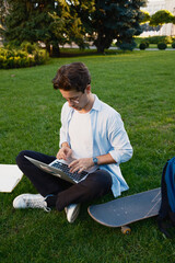 A young individual seated on grass with a laptop, accompanied by a skateboard, signifying work and...