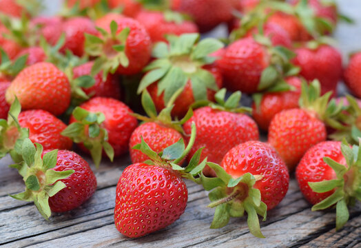 Fresh strawberries spread out on a rustic wooden table surface