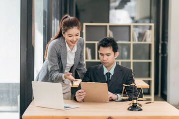 Lawyers discuss contract documents at a wooden table. Symbols of justice are hammer and scales, giving legal advice in a courtroom to clients.