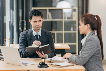 Lawyers discuss contract documents at a wooden table. Symbols of justice are hammer and scales, giving legal advice in a courtroom to clients.