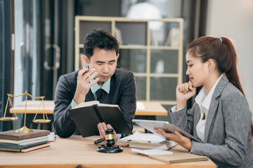 Lawyers discuss contract documents at a wooden table. Symbols of justice are hammer and scales, giving legal advice in a courtroom to clients.