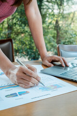 Close-up of a person reviewing financial reports with charts and graphs, using a laptop in a...