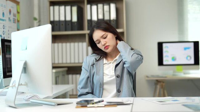 Professional businesswoman experiencing neck and shoulder pain while working on laptop, demonstrating physical discomfort from sedentary workplace environment