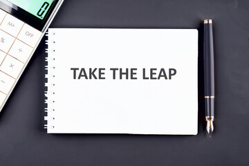 TAKE THE LEAP WORDS WRITTEN on a white notebook sheet on a graphite background