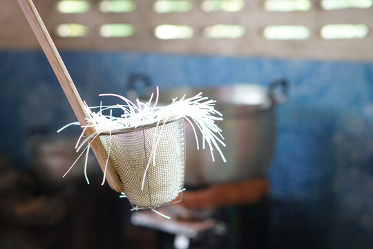 Noodle strainer with rice noodles, used for blanching in hot water. Concept, essential kitchen tool for preparing authentic Asian cooking, ensuring perfect, silky noodles every single time.