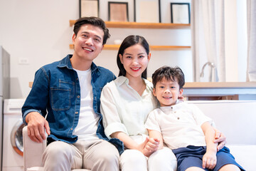 Happy family of three: parents and child smiling together on a sofa in their well-lit home