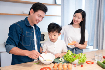 Asian family preparing healthy meal together at home father stirring eggs with son cutting vegetables