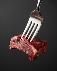 A photograph of a stainless steel fork piercing a thick slab of raw, marbled beef