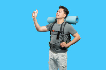 Fototapeta premium Man spraying sanitizer before outdoor adventure sporting backpack and rolled up mat against blue backdrop