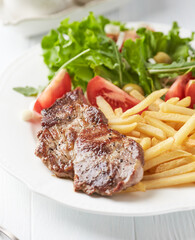Grilled Steak with french fries and fresh salad. White wooden background.	