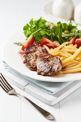 Grilled Steak with french fries and fresh salad. White wooden background.	