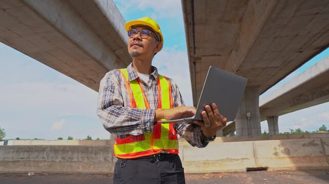 A seasoned bridge engineer meticulously inspects a modern concrete overpass while reviewing technical data on his laptop. The focus on expertise.