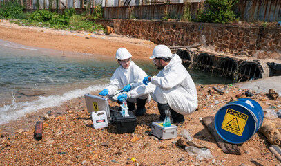 Scientists biologists and researchers in protective suits taking water samples from waste water...