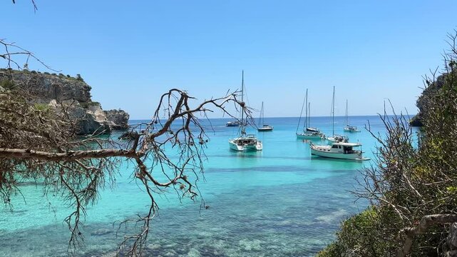 Boats floating on the crystal-clear turquoise waters near Cala Macarella beach in Menorca, Spain, surrounded by stunning cliffs and lush green trees, creating a picturesque Mediterranean paradise.