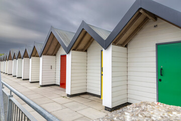 Row of white wooden beach huts with bright colorful doors in spring in quay with cloud sky in background in Swanage, UK. South coast of England, Dorset. Cold weather. Nobody