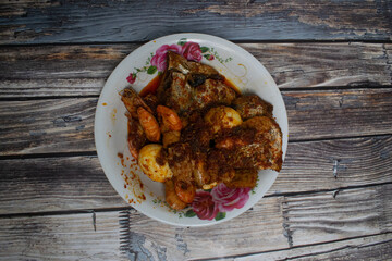 A traditional dish featuring spicy prawns, boiled eggs, fried fish and tempeh on a flower plate.