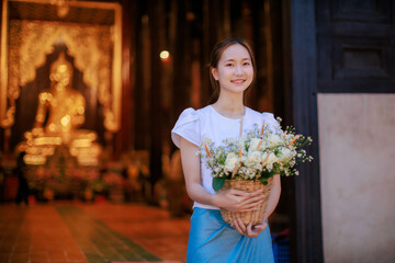 beautiful Thai woman holding flower basket worship Chiang Mai City Pillar Inthakin Festival, crowd buddhist people make merit with flowers in Wat Chedi Luang temple at night