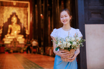 beautiful Thai woman holding flower basket worship Chiang Mai City Pillar Inthakin Festival, crowd buddhist people make merit with flowers in Wat Chedi Luang temple at night