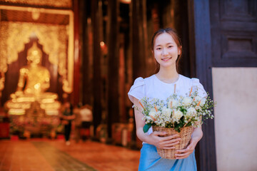 beautiful Thai woman holding flower basket worship Chiang Mai City Pillar Inthakin Festival, crowd buddhist people make merit with flowers in Wat Chedi Luang temple at night