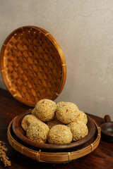 High-resolution image of onde-onde, traditional Indonesian sesame balls made from glutinous rice flour filled with mung bean paste. The snack is beautifully arranged on a clay plate with rustic bamboo