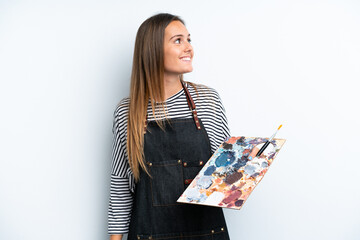 Young artist caucasian woman holding a palette isolated on white background looking side