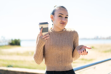 Young moroccan girl holding a take away coffee at outdoors making doubts gesture while lifting the...