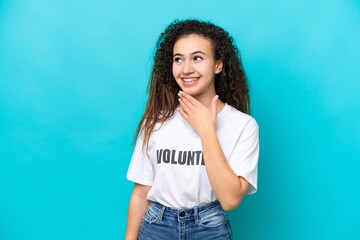 Young Arab volunteer woman isolated on blue background looking up while smiling