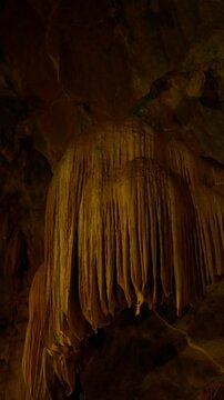 Close-up view of dramatic cave formations with intricate limestone drapes illuminated by warm lighting, showcasing geological features and natural subterranean beauty.