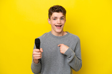 Singer Teenager man picking up a microphone isolated on yellow background with surprise facial...