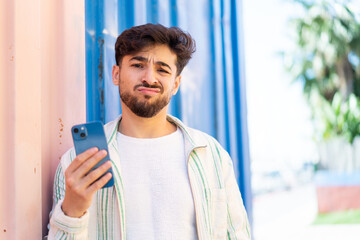 Handsome Arab man using mobile phone at outdoors with sad expression