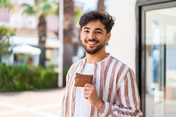 Handsome Arab man holding a wallet at outdoors smiling a lot