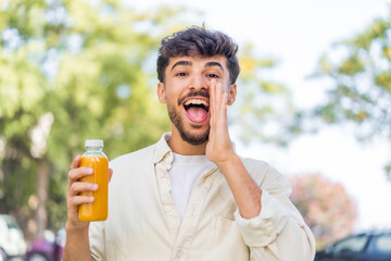 Fototapeta premium Young Arabian handsome man holding an orange juice at outdoors shouting with mouth wide open